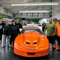 Industry colleagues gathered around an orange performance car